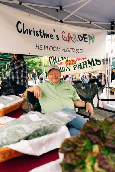 A farmer sitting at a market booth under a banner for 