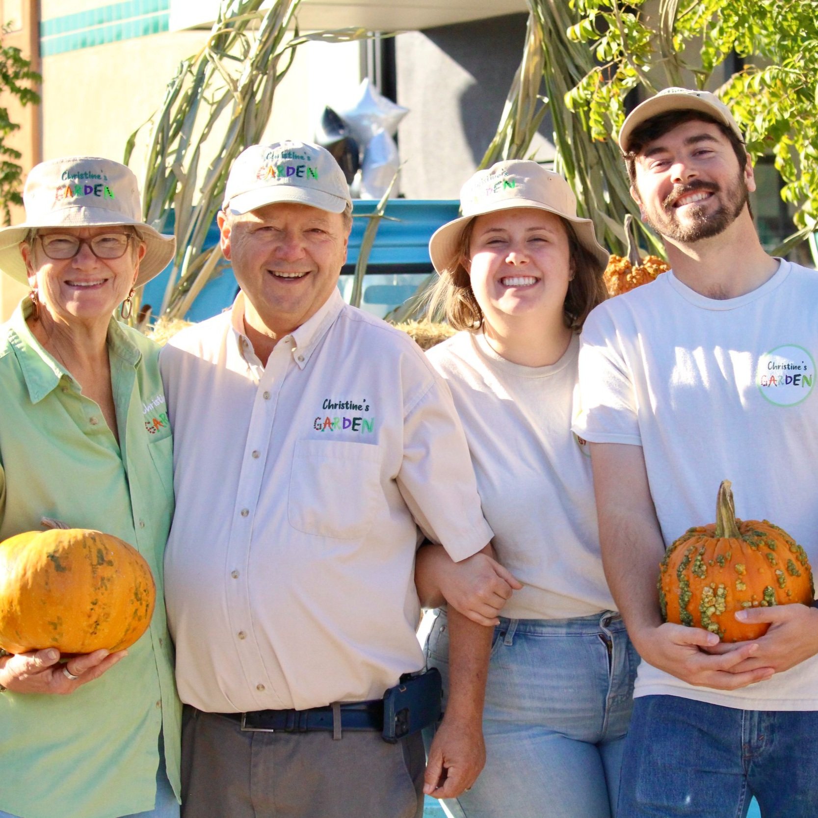 Christine's+Garden,+California+-+IMG_4284 Family members pose together at Christine's Garden, wearing matching hats and holding pumpkins, with a backdrop of hay and greenery, celebrating the harvest season.